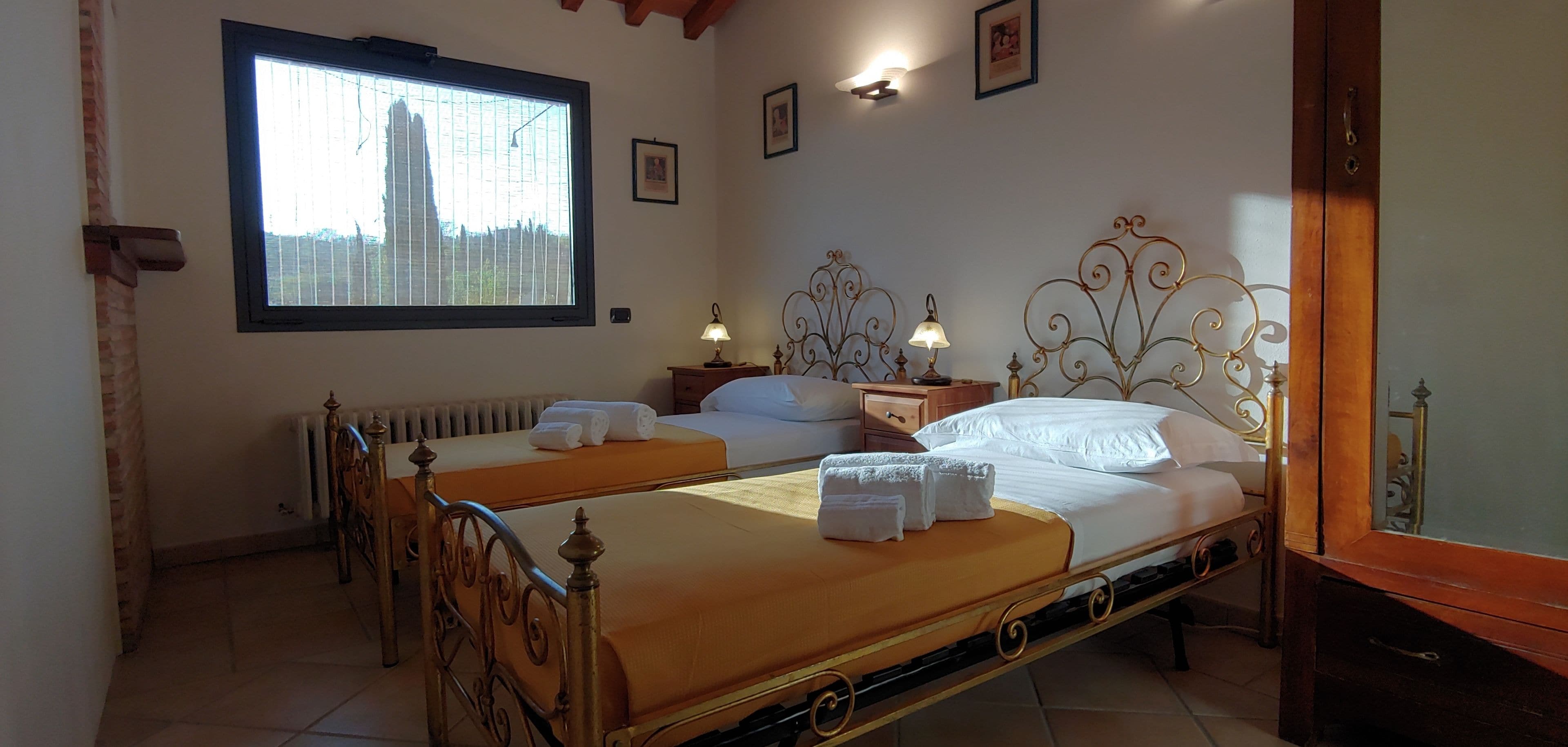 A room with two beds, a window with blinds, a radiator, and wall-mounted lights.