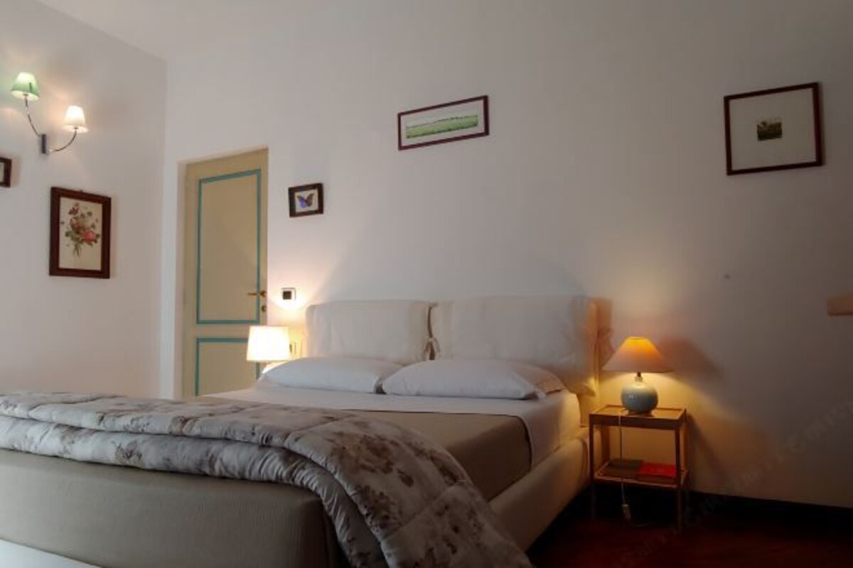 A bedroom with a bed, bedside lamps, and framed pictures on the wall.