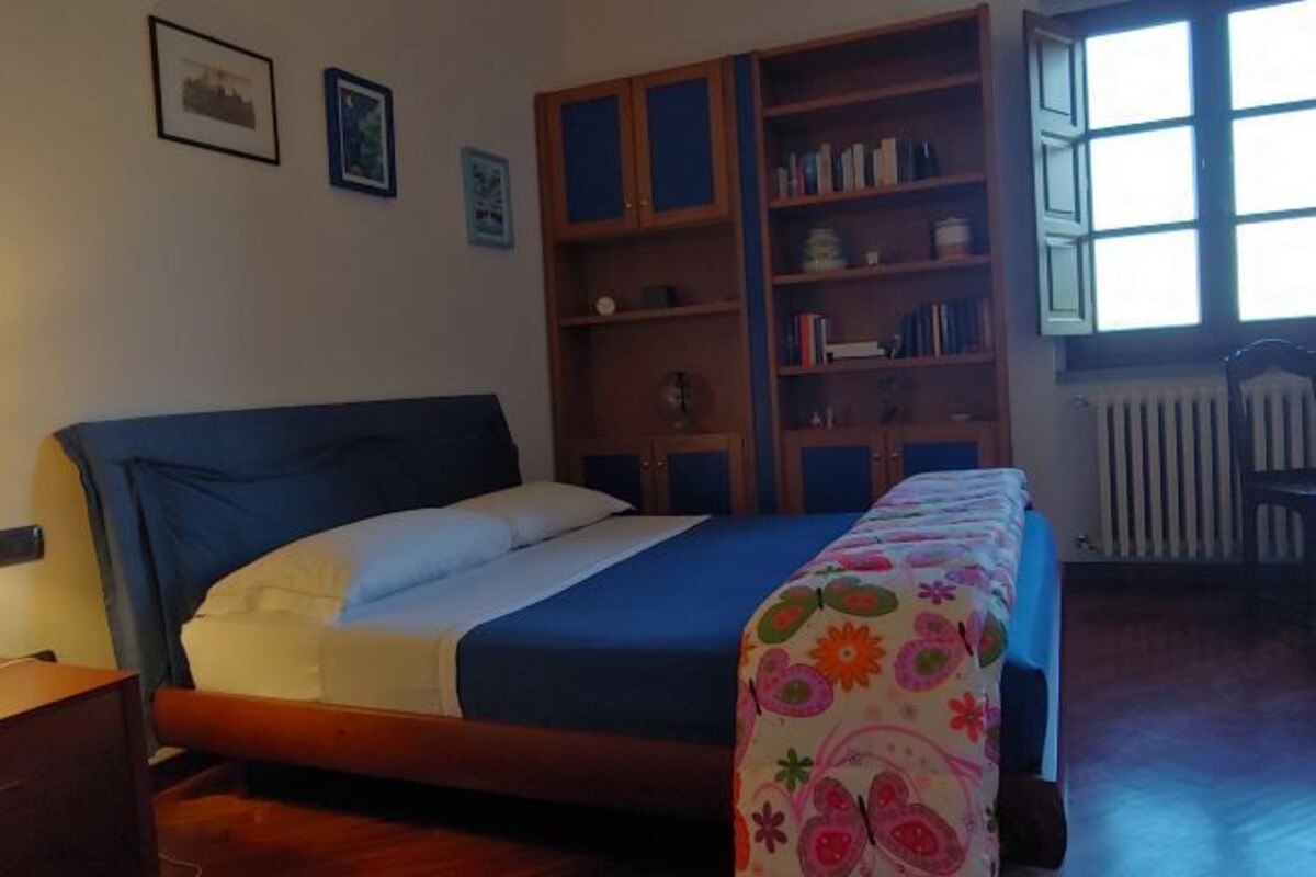A bedroom with a bed, a wooden bookshelf, and a window with blinds.