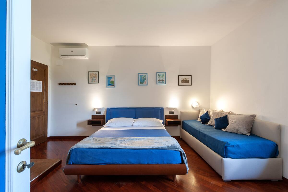A bedroom with a bed, a sofa, a wooden floor, and wall-mounted artwork.