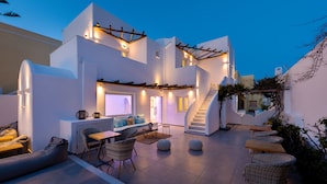 Un espacio exterior moderno con sofá, sillas y una mesa, rodeado de muros blancos y una escalera.