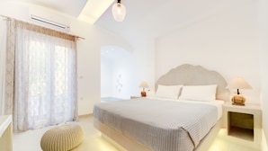 Un dormitorio moderno con una cama grande, mesitas de noche con lámparas, un cabecero decorativo y un ventanal con cortinas traslúcidas.