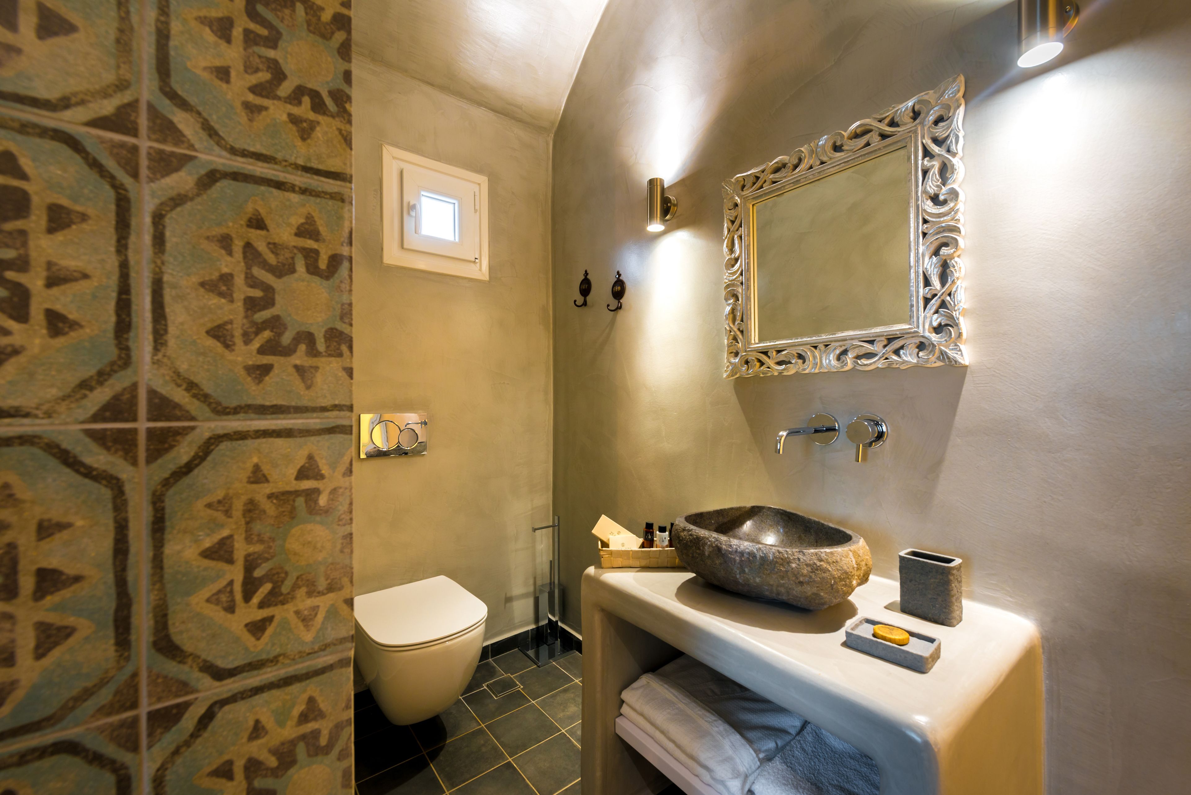 A bathroom with a stone sink, a toilet, and patterned tiles.