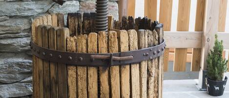 Een rustieke houten vat met een metalen mechanisme, voor een stenen muur en houten hek.