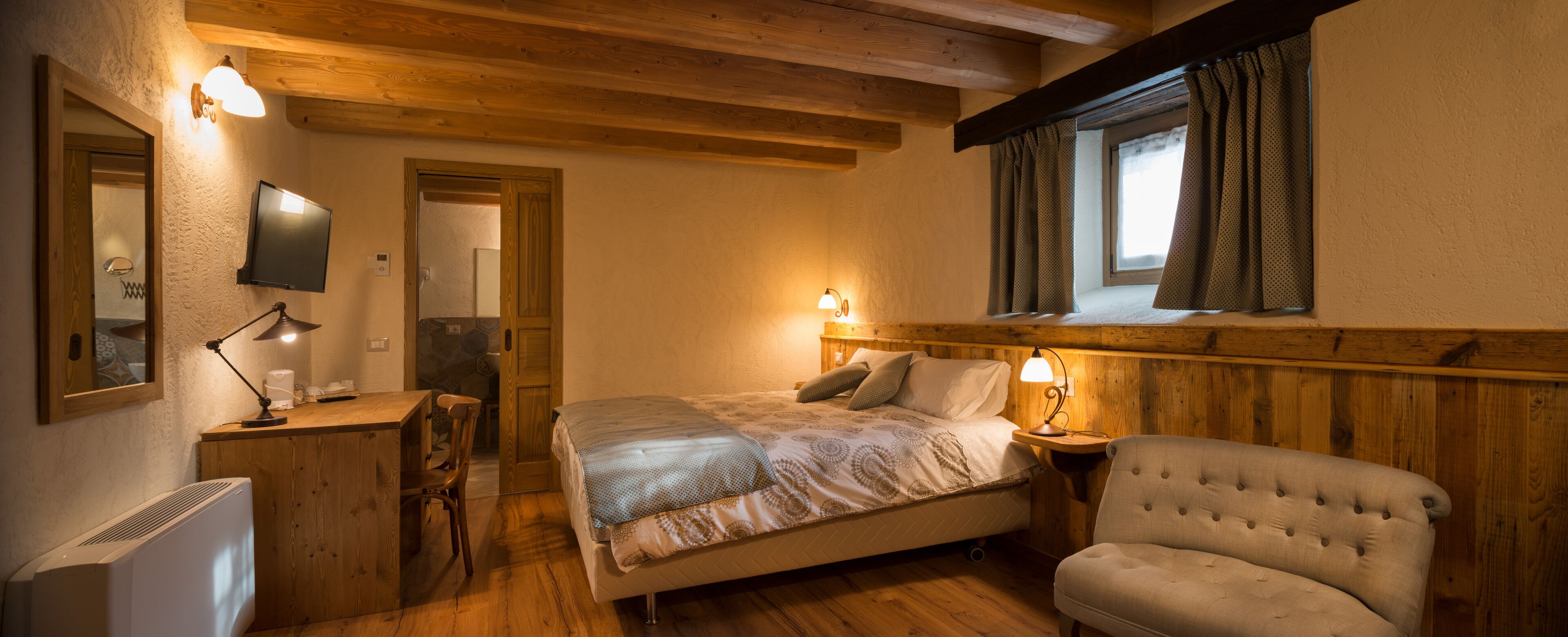 A cozy bedroom with a bed, bedside table, chair, and a TV mounted on the wall.