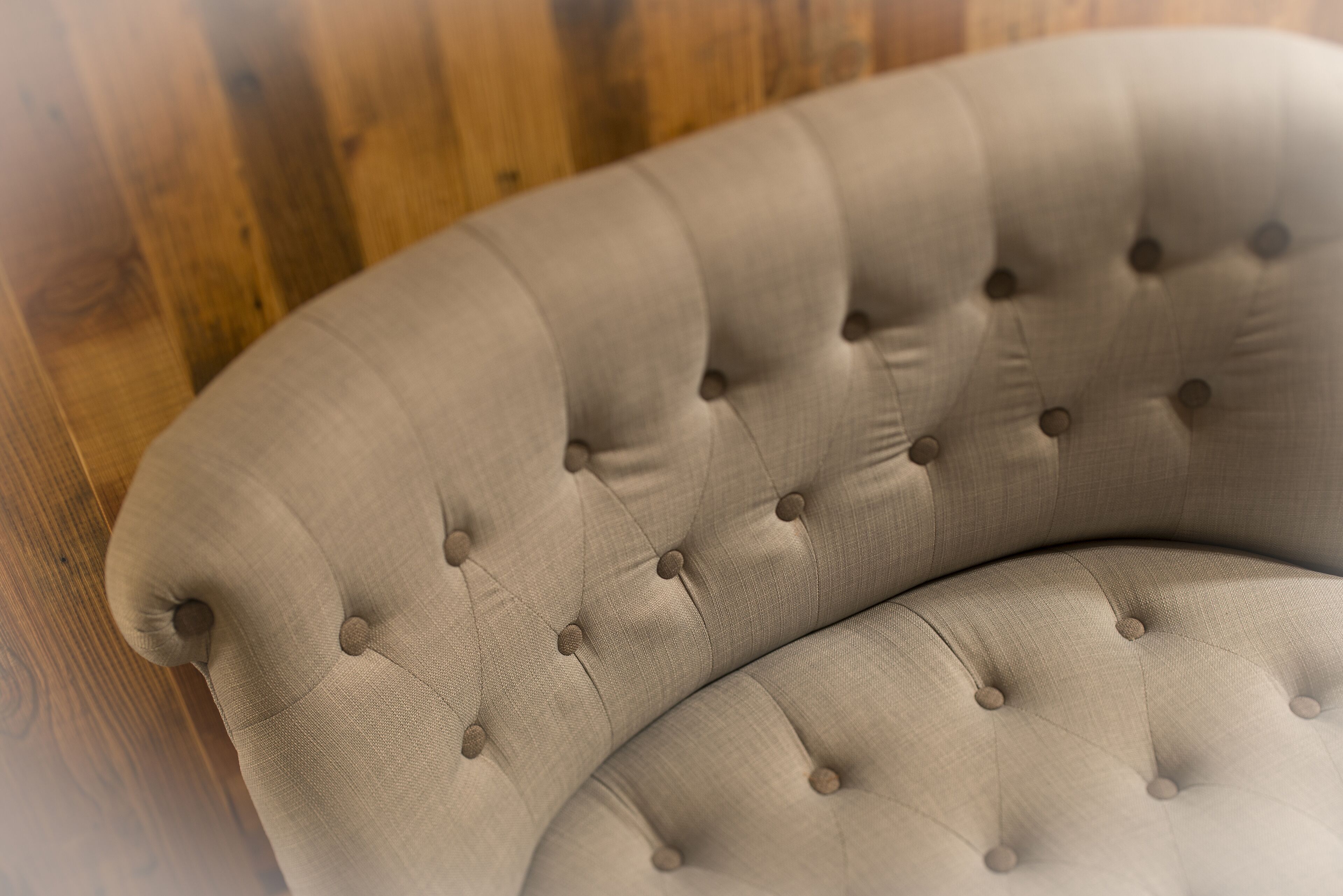 A tufted sofa with a curved design, upholstered in a light fabric, positioned against a wooden background.