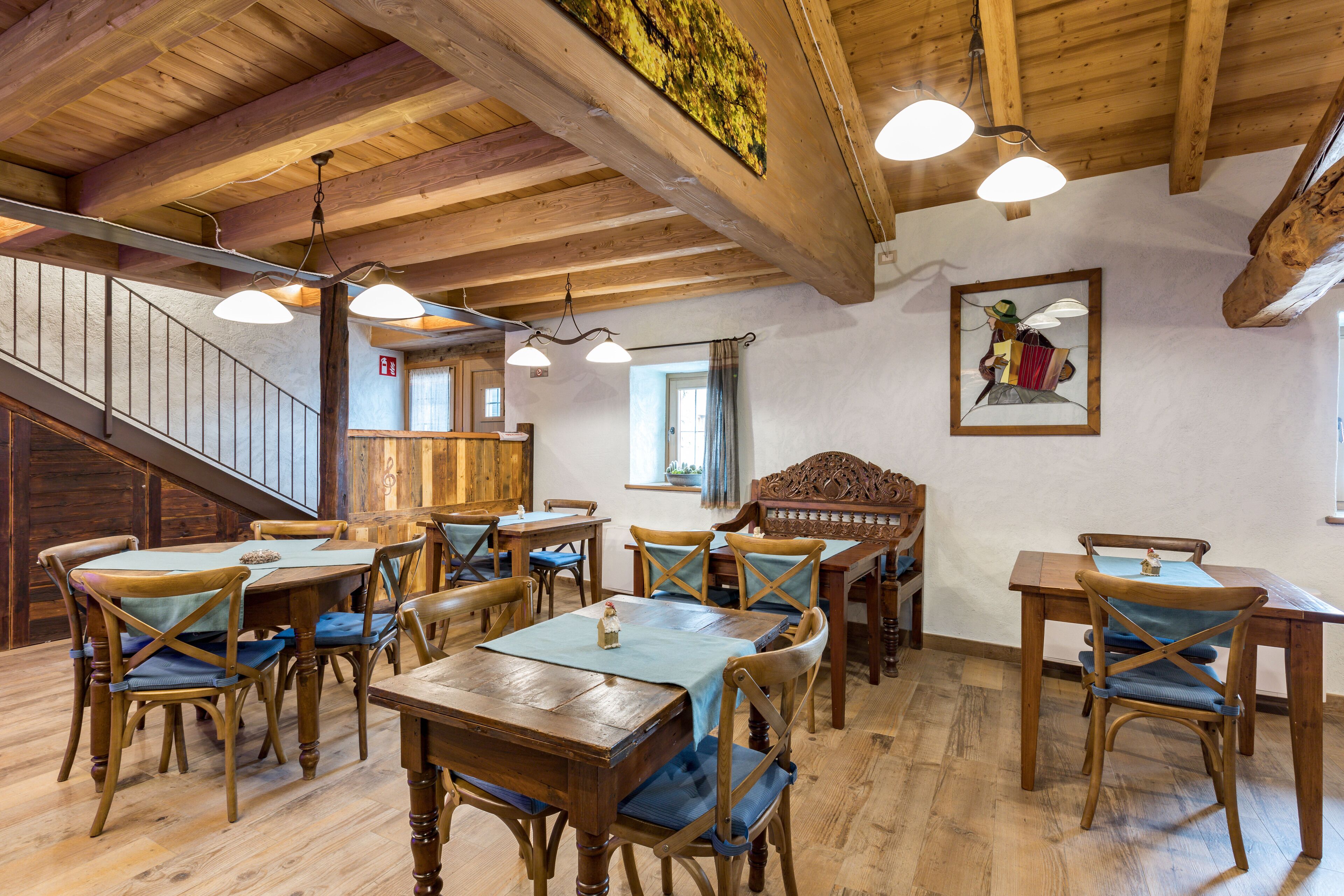 A wooden interior with tables and chairs, a staircase, and a painting on the wall.