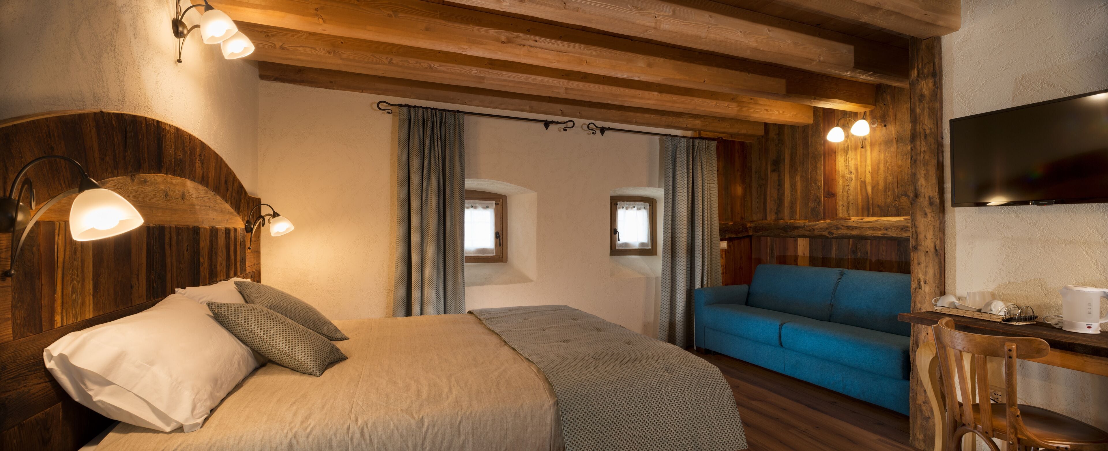 A cozy room with a bed, a blue sofa, and a TV.
