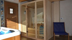 Una sauna de madera con puertas de vidrio, un banco de madera y una silla azul en un espacio con piso de madera y una puerta de madera.