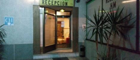 A hotel entrance with a reception area, a sign indicating 'Hostal Mari Loli - Recepcion', and a sign for 'Recepcion HM'.