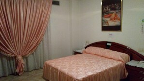 A bedroom with a bed, a nightstand, a wall-mounted painting, and a curtain. - Hostal Mari Loli (San Fulgencio)