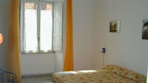 Ein Schlafzimmer mit Bett, einem Fenster mit Vorhängen, einer Wandsteckdose und einem kleinen Bild.