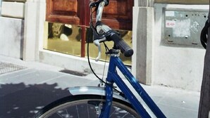 Ein blaues Fahrrad steht vor einem Gebäude mit einer großen Holztür und einem Briefkasten an der Wand.