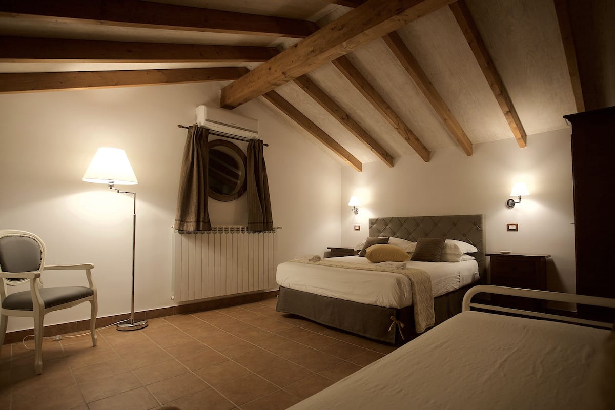 Un dormitorio con cama, mesitas de noche, una silla y una lámpara de pie.