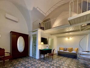 A room with a patterned floor, a wooden cabinet, a desk with a lamp, a sofa with cushions, and a staircase with a railing. - Villa Scinata Historic House (Nardò)