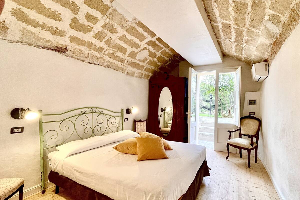 Un dormitorio con una cama, una silla, un espejo y una puerta que da al exterior.