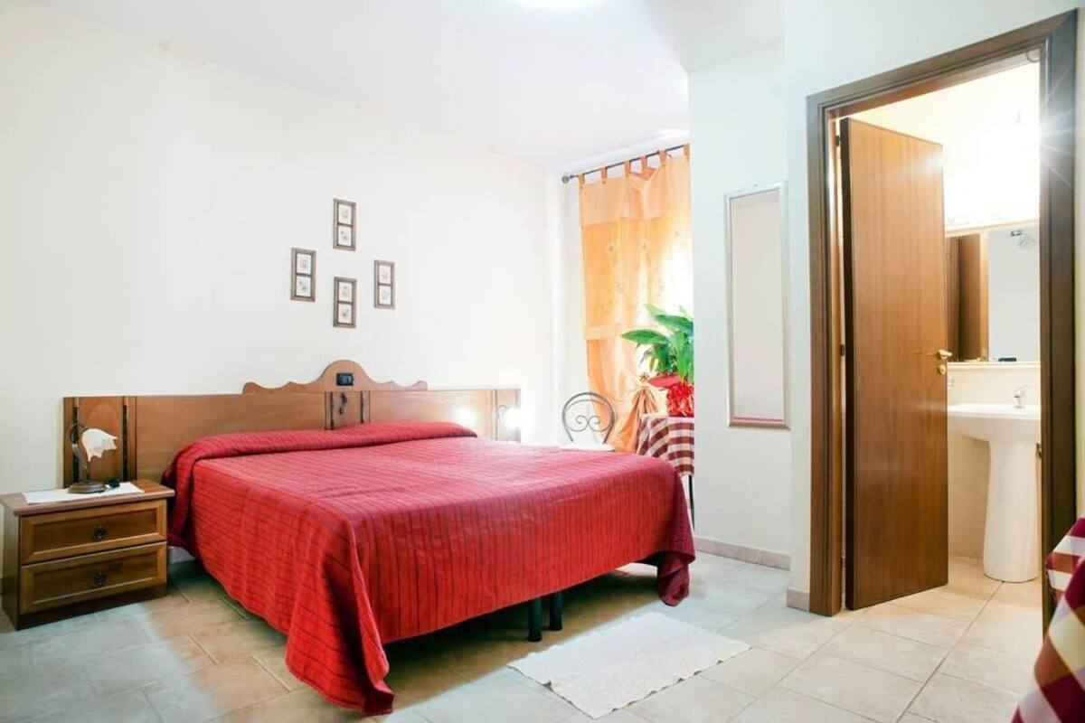 Ein Schlafzimmer mit einem hölzernen Bett, einem Nachttisch, einem Schminktisch, einem Spiegel, einem Fenster mit Vorhängen und einer Tür, die ins Bad führt.