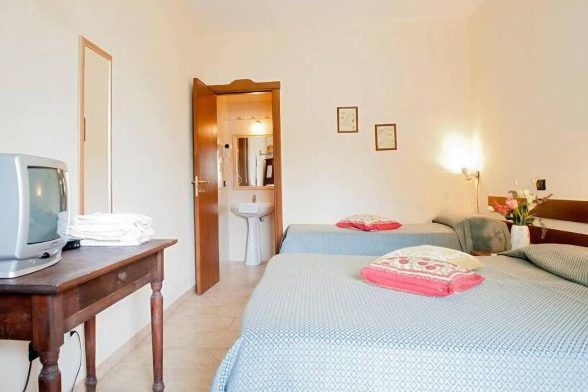 Ein Hotelzimmer mit einem Bett, einem Nachttisch mit Fernseher, einem Spiegel, einem Waschbecken und zwei gerahmten Bildern an der Wand.