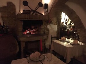 A rustic dining area with a stone fireplace, wooden furniture, and a table set for two. - Hotel il Malandrone (Castellina Marittima)