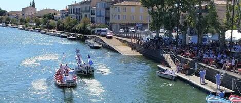 Un río con barcos, una multitud en la orilla y edificios al fondo.