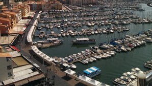 A marina with numerous boats docked, a promenade with buildings, and a clear view of the sea. - Hôtel Araur (Agde)