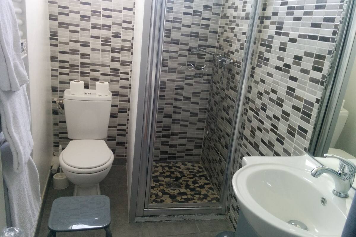 A bathroom with a toilet, a shower with a tiled wall, and a sink.