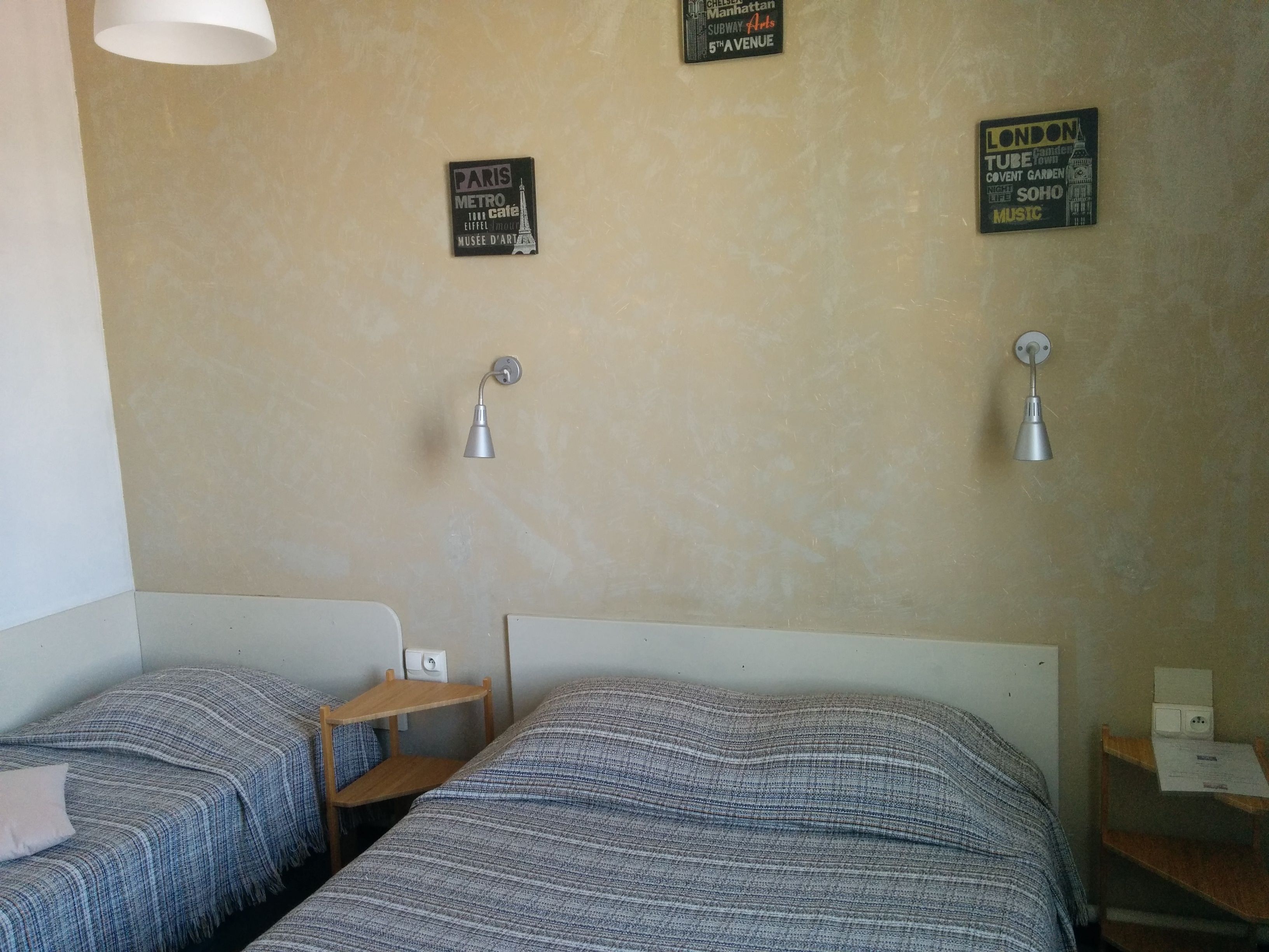 Une chambre avec deux lits, une lampe fixée au mur et deux panneaux publicitaires pour le Paris Metro Café et le London Tube.