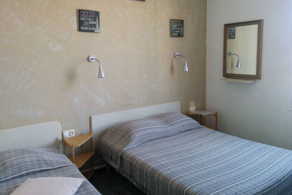 A hotel room with two single beds, a small wooden nightstand, a wall-mounted lamp, and a mirror.