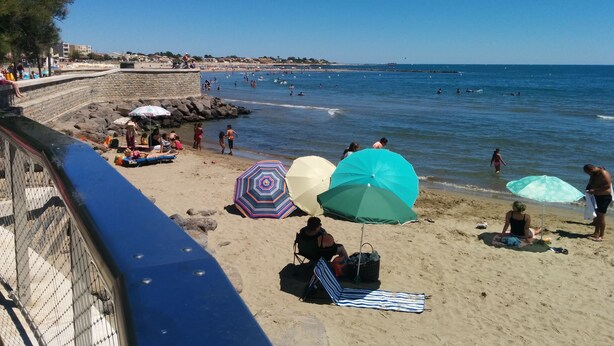 A beach with people sunbathing and swimming, umbrellas, and a rocky breakwater. - Hôtel Araur (Agde)