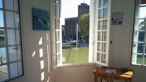 A room with a large window overlooking a canal, a wooden chair, and a small table. - Hôtel Araur (Agde)