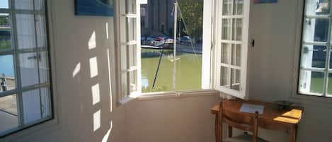 A room with a large window overlooking a canal, a wooden chair, and a small table.