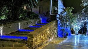 A nighttime outdoor area with stone steps leading up to a building, illuminated by blue lights. - Hôtel Araur (Agde)