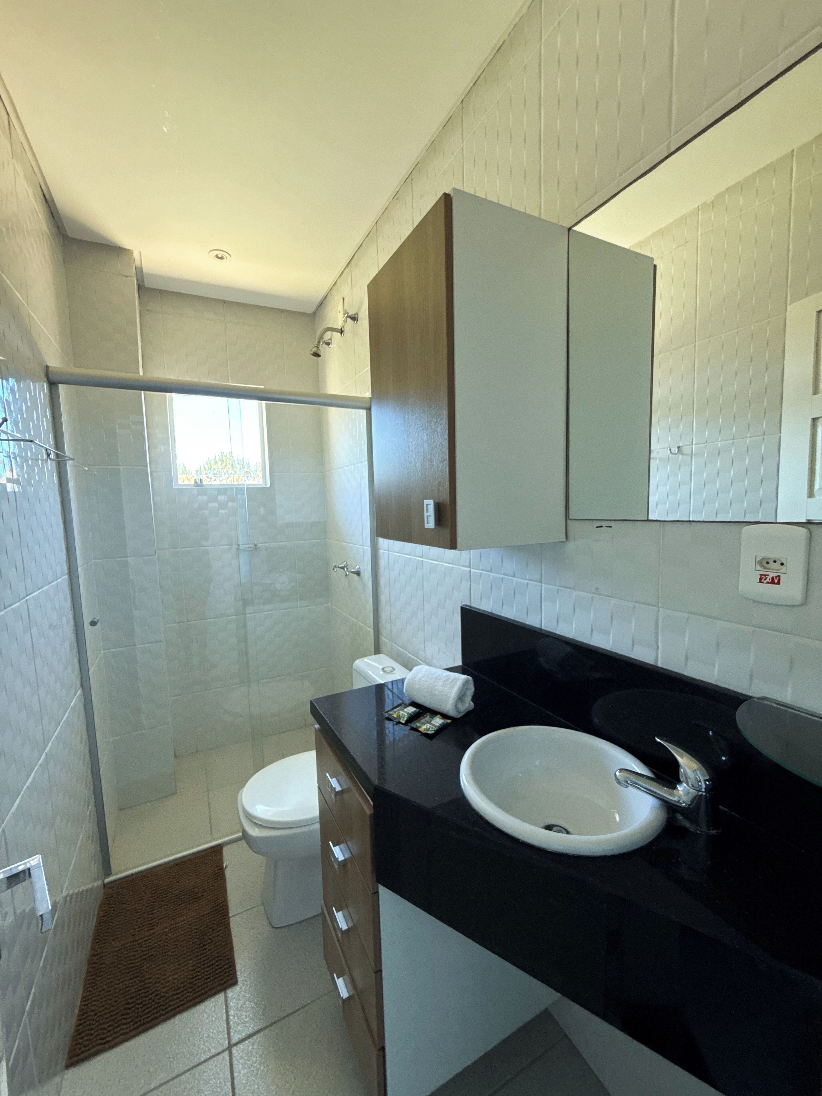 Uma casa de banho moderna com chuveiro de vidro, sanita, lavatório com espelho e um porta-toalhas.