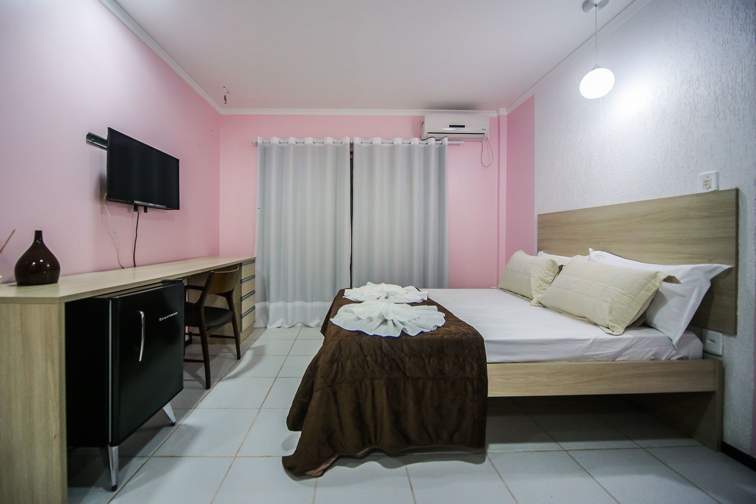 A bedroom with a bed, a desk, a chair, a TV, and an air conditioning unit.