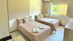 A hotel room with two beds, a dining table, and a window with a view of greenery. - Hotel Pousada Laguna Rosa (Imbituba)