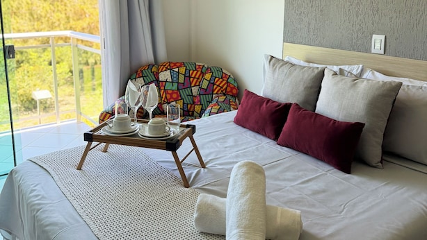 A modern bedroom with a large bed, a balcony view, a ceiling fan, and a red pendant light. - Hotel Pousada Laguna Rosa (Imbituba)