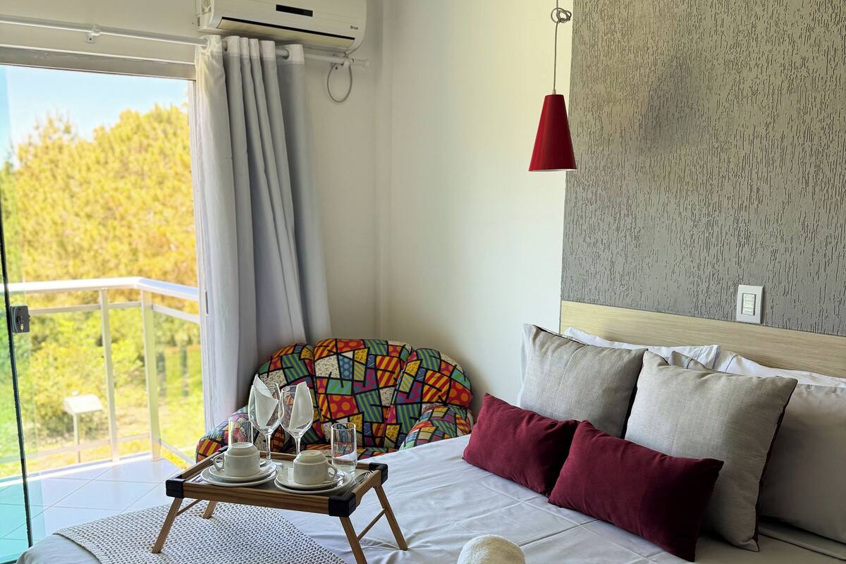 Une chambre moderne avec un grand lit, une vue sur le balcon, un ventilateur de plafond et un luminaire suspendu rouge.