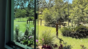 A view through a window of a park with trees, grass, and a bench. - Hotel Pousada Laguna Rosa (Imbituba)