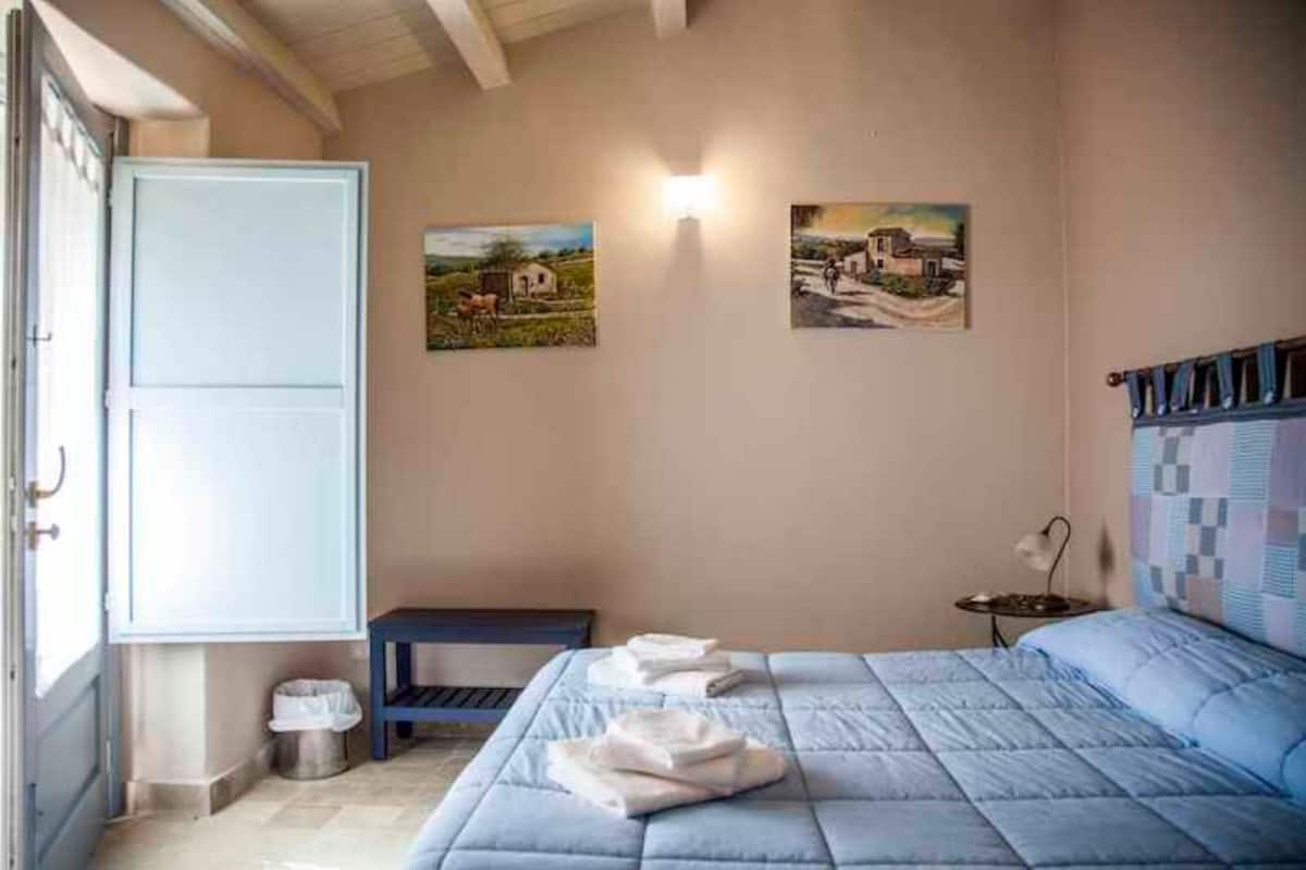 A bedroom with a bed, a bedside table, a lamp, and two paintings on the wall.