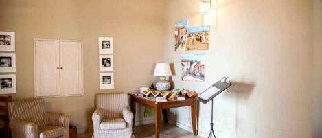 A living room with a piano, a lamp, and framed pictures on the wall.