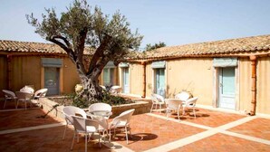 A courtyard with outdoor seating and a large tree. - Avola Antica (Avola)