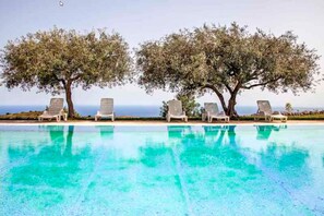 A pool with clear blue water, surrounded by lounge chairs and two large trees. - Avola Antica (Avola)