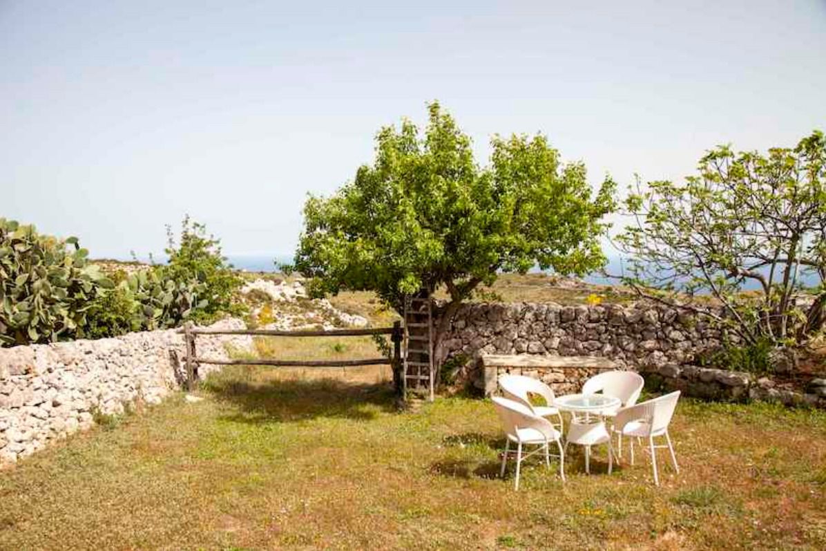 Un patio con sillas blancas y una mesa, un muro de piedra y un árbol.