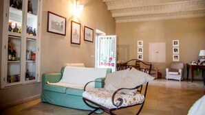 A living room with a teal sofa, a patterned armchair, a cabinet with bottles, and framed pictures on the wall. - Avola Antica (Avola)