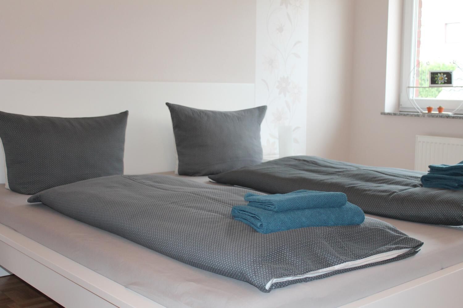 A bed with grey bedding and a folded blue towel.