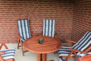 Une table en bois, quatre chaises à rayures, une petite plante en pot et un mur en briques en arrière-plan.