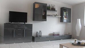Una sala de estar moderna con una televisión de pantalla plana sobre un mueble, un espejo grande y un diseño minimalista.