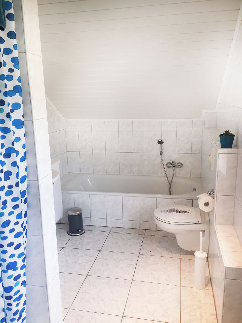 A bathroom with a bathtub, toilet, and a trash bin.