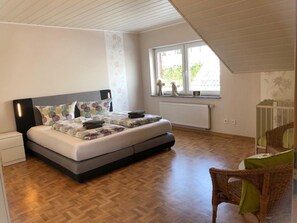 Une chambre à coucher avec un lit, une fenêtre, un radiateur et une chaise en osier.