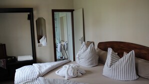 A neatly made bed with striped bedding, a wooden headboard, and a large mirror on the wall. - Hotel zum Ginkgobaum (Stadtilm)